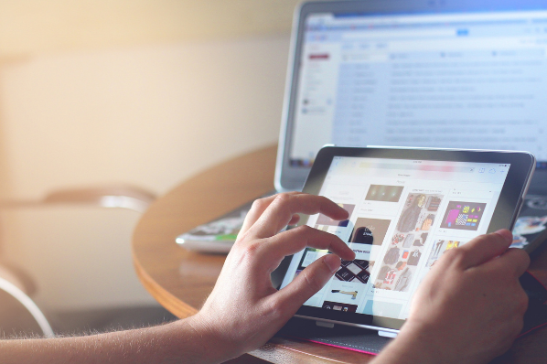 personne sur sa tablette avec un ordinateur ouvert en arrière plan