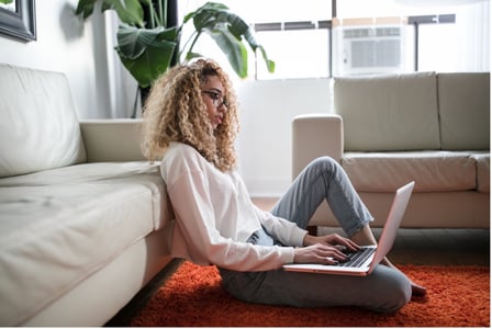 femme sur son PC assise par terre dos à son canapé
