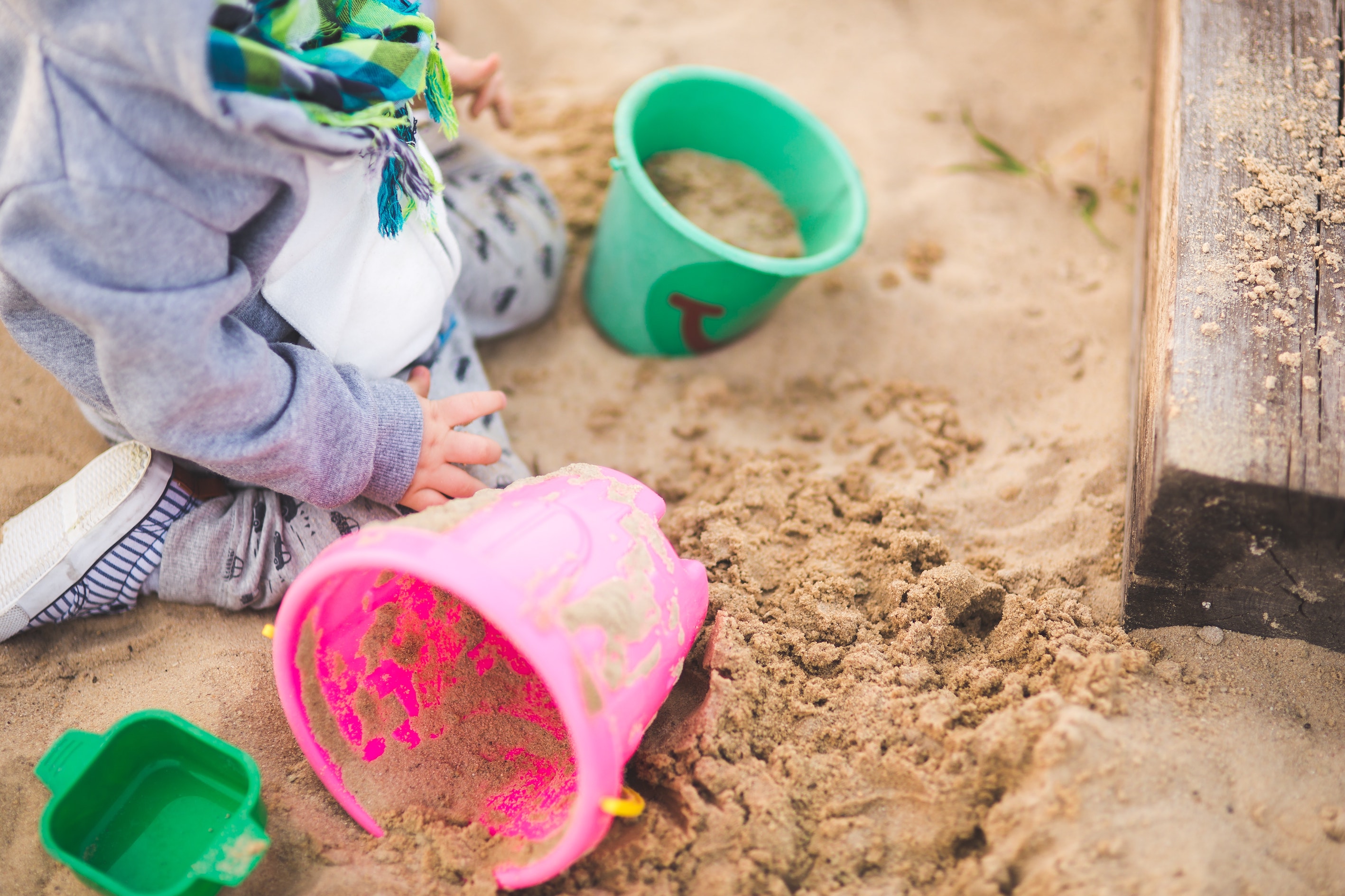 enfant dans un bac à sable jouant avec deux seaux
